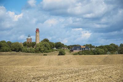 Lighthouse on field by buildings against sky