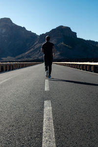 Rear view of man standing on road against mountain range