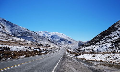 Road amidst snowcapped mountains against clear blue sky