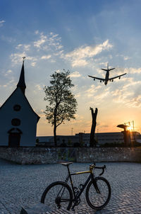 Bicycle by tree against sky during sunset