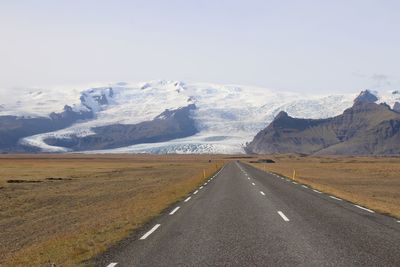 Empty road leading towards snowcapped mountains against sky