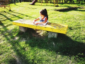 High angle view of girl doing homework on table while sitting on grassy field in park