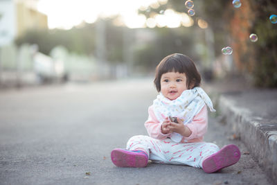 Cute girl looking at bubbles while sitting on road