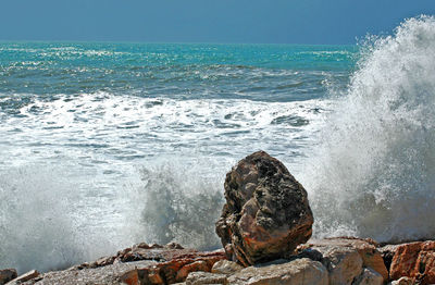 Waves splashing on rocks at shore against sky