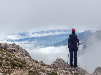 Rear view of female hiker standing on mountain against sky during winter