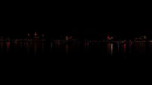 Illuminated buildings by river against clear sky at night