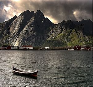 Boat moored on sea by mountain against sky