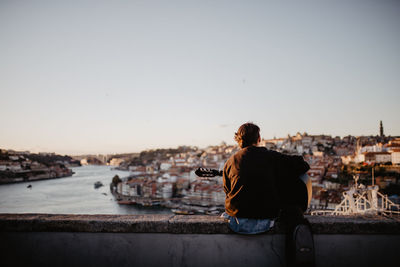 Rear view of man with guitar looking at cityscape against sky