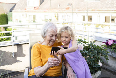 Granddaughter showing mobile phone to grandmother in balcony