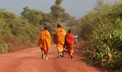Rear view of monks walking on road amidst trees