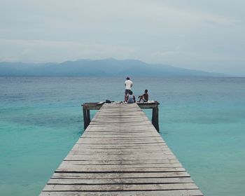 Men on pier by sea against sky