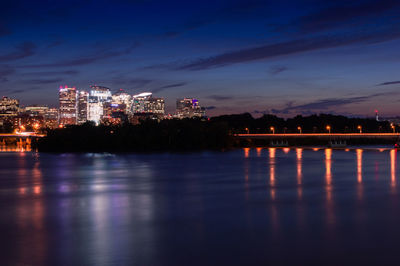 Illuminated buildings by river against sky at night