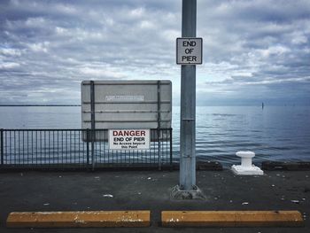 Warning sign on sea against cloudy sky