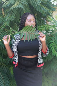 Young woman with arms raised standing against plants