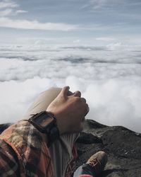 Low section of man relaxing on mountain against cloudscape