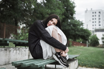 Thoughtful woman hugging knees while sitting on bench at park