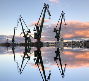 Low angle view of cranes by lake against sky during sunset 