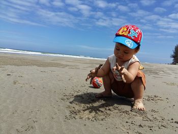 Close-up of baby boy playing with sand at beach against sky