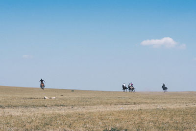 People riding horses on field against sky