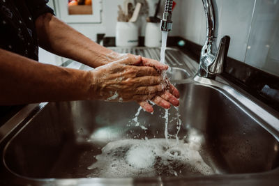 Midsection of man washing hands in sink