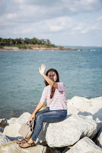 Portrait of young woman sitting by sea against sky