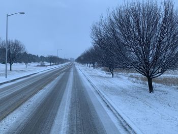 Snow covered road by bare trees against sky
