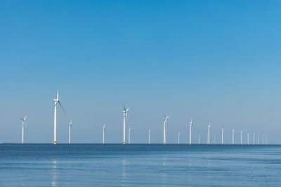 Wind turbines by sea against clear blue sky, 