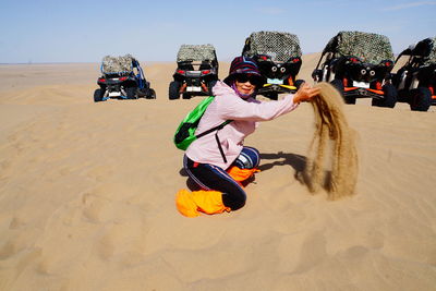 Side view portrait of woman playing with sand at desert