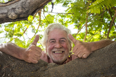 Portrait of smiling senior man showing thumbs up on tree