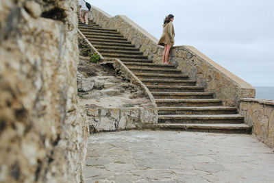 Low angle view of woman standing on staircase while looking at sea