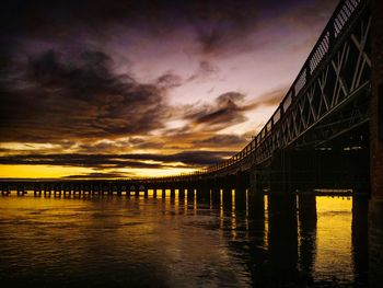 Silhouette bridge over river against sky during sunset