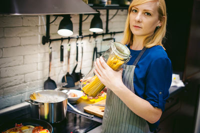 Portrait of woman holding raw pasta in jar at kitchen