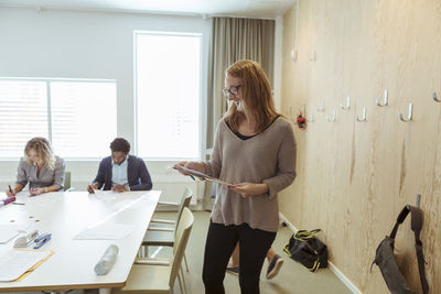 Smiling businesswoman reading document while colleagues working in background at conference table