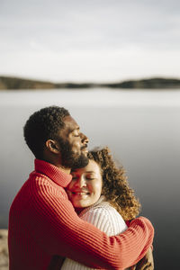 Heterosexual couple embracing by lake on sunny day
