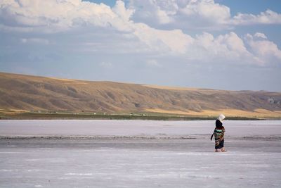 Full length of woman in hijab walking on frozen river against cloudy sky