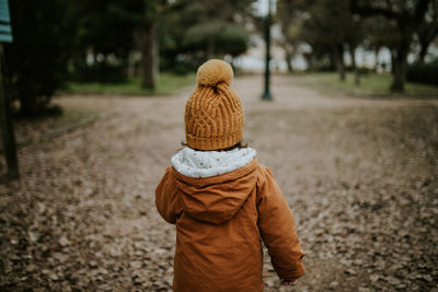 Rear view of girl walking on footpath in park during winter