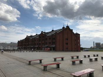 Empty benches on footpath by buildings in city against sky