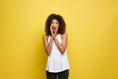 Portrait of young woman surprised against yellow background