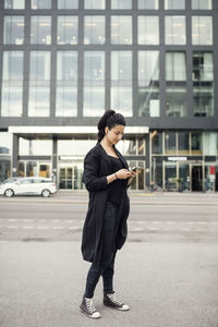 Woman using mobile phone against building in city