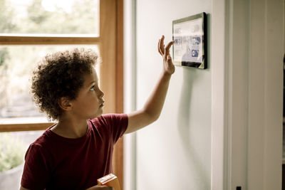 Boy with curly hair using home automation system mounted on wall