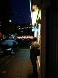 Side view of mid adult woman standing on sidewalk at night