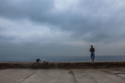 Rear view of woman standing on beach against cloudy sky