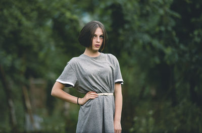 Young woman looking away while standing against trees