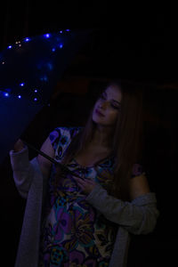Young woman looking away while standing against black background
