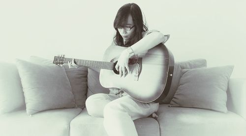 Woman playing guitar while sitting on sofa at home