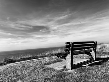 Empty bench on field against sky