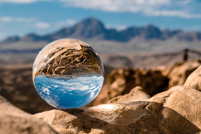 Close-up of crystal ball on rock against sky