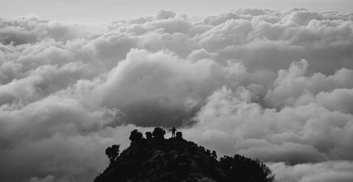 Person on mountain against cloudy sky