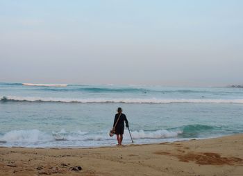 Rear view of man standing on shore at beach against sky