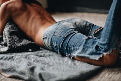 Midsection of shirtless woman lying on floor at home